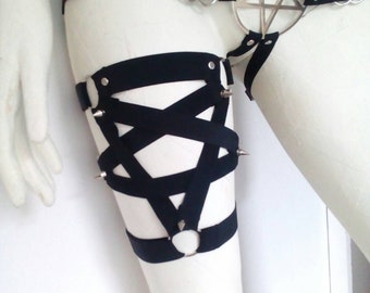 May include: Black harness with a pentagram design. The harness features a large metal pentagram, metal rings, and studded accents. The harness is worn on a mannequin.