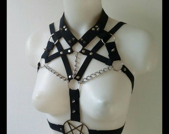 May include: Black harness with a pentagram pendant. The harness features silver metal rings, chain accents, and studded details. The design includes straps across the chest and shoulders, creating a bold and edgy aesthetic.