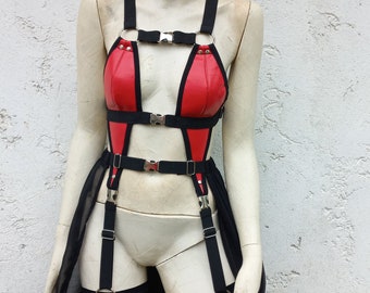 May include: A red and black harness set featuring a red choker with a metal buckle, a red chest piece with black trim, and black elastic straps connected by silver-toned metal buckles and rings, with a long black sheer fabric skirt attachment.