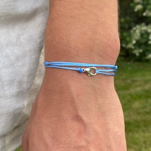 Può includere: Un braccialetto blu chiaro con una chiusura argentata. Il braccialetto è composto da due fili di cordoncino.