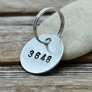 May include: A circular silver-coloured metal tag featuring the stamped black numbers 3648. The tag includes a small hole at the top with a silver-coloured metal split ring attached, designed for use as a keyring or identification tag for personal items.