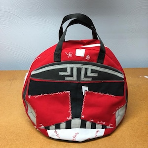 May include: Red and black fabric bag with a white and gray design resembling a helmet. The bag has a black handle and is made of a patchwork of different fabrics.