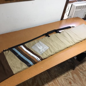 May include: A tan and brown canvas bag with a black strap and a white logo that says "Snow Wolf". The bag has a striped pattern on the front.