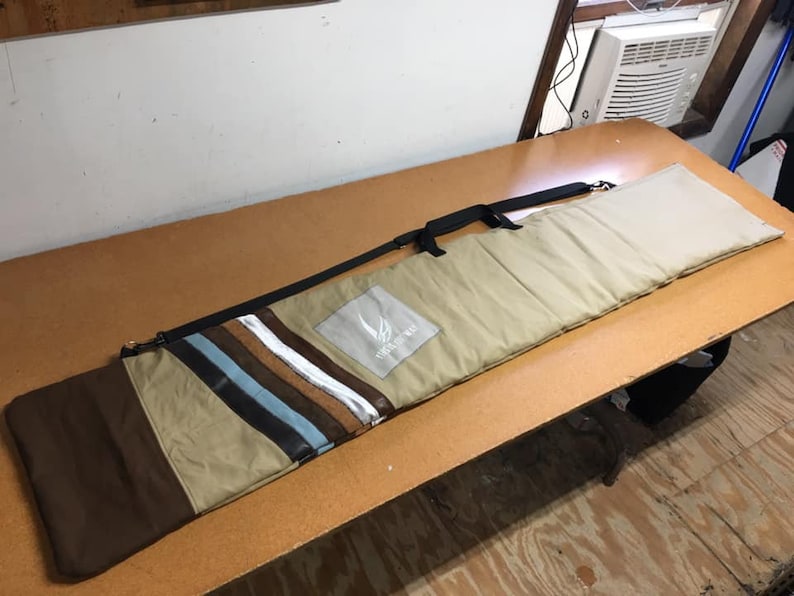 May include: A tan and brown canvas bag with a black strap and a white logo that says "Snow Wolf". The bag has a striped pattern on the front.