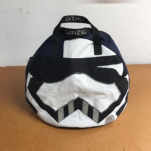 Puede incluir: Una bolsa de lona azul marino y blanca con una correa negra y un diseño de Stormtrooper blanco. La bolsa tiene el texto "TK21470" y "07415KT" impreso en la correa.