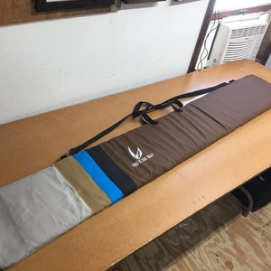 May include: A brown canvas bag with a black strap and a white logo that says "The Way of the Way". The bag has a multi-colored stripe design in tan, blue, and black.