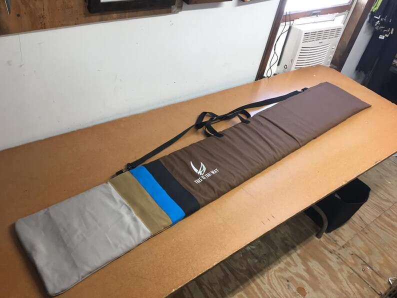 May include: A brown canvas bag with a black strap and a white logo that says "The Way of the Way". The bag has a multi-colored stripe design in tan, blue, and black.