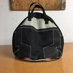May include: A black and gray round bag with a single handle. The bag has a white lining and red accents.