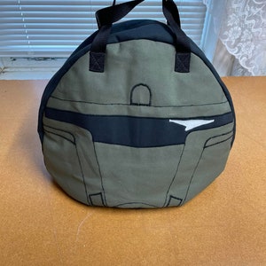 May include: A green and black canvas bag with a white design. The bag has a single handle and a rounded shape.