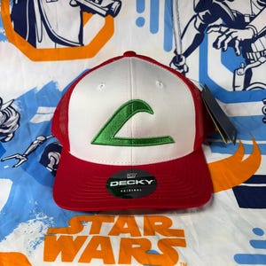 Könnte beinhalten: Eine rot-weiße Baseballkappe mit grünem Logo. Die Kappe hat einen Mesh-Rücken und einen gebogenen Schirm. Der Markenname "DECKY" ist auf einem schwarzen Aufkleber zu sehen. Die Kappe befindet sich auf einem Star Wars-Hintergrund.