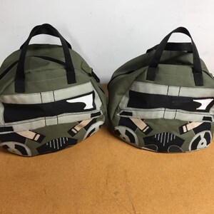 May include: Two green canvas duffel bags with black straps and a black and white graphic of a stormtrooper helmet on the front.