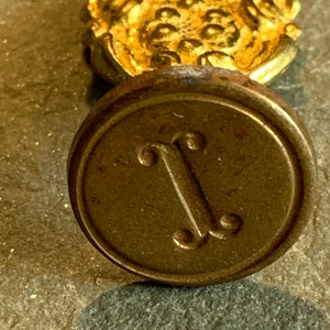 May include: A brass seal with a decorative design and the letter "J" embossed in the center.