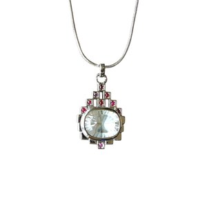 Può includere: Collana color argento con un pendente con una grande pietra ovale iridescente. Il pendente è impreziosito da piccole pietre rosa quadrate e da un design geometrico. La collana è appesa a una catena sottile.