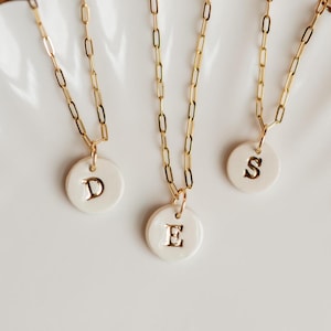 May include: Three gold chain necklaces with white ceramic pendants. Each pendant has a gold letter, D, E, and S.