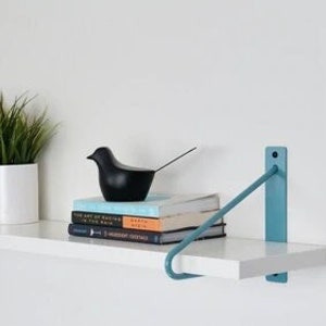 May include: A white shelf with a blue metal bracket. The shelf is decorated with a framed photo, a potted plant, a small black bird figurine, and a stack of books.