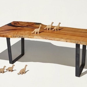 May include: A wooden table with a live edge top and black metal legs. There are five small dinosaur figurines on the table.
