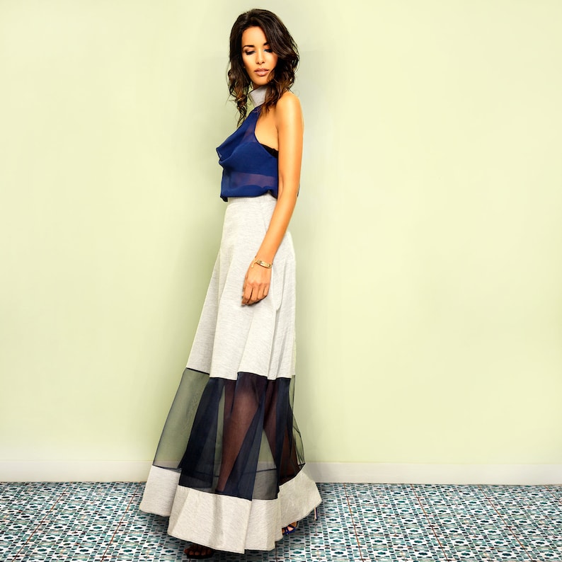 May include: A woman wearing a navy blue halter top with a white and black layered skirt. The skirt has a sheer overlay and a white waistband.