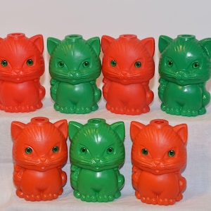 May include: Set of six plastic cat figurines, three red and three green. The cats are all in a sitting position with their tails curled around their legs.