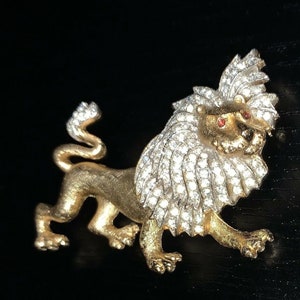 Op de afbeelding: Een gouden leeuwen broche met rode strass steentjes als ogen en een manen van heldere strass steentjes.