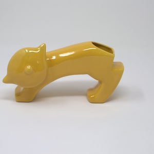 May include: A yellow ceramic cat figurine with a hollowed-out back, designed to be used as a vase or planter.