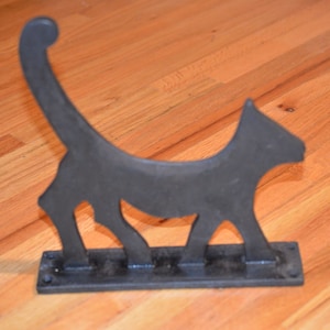Puede incluir: Tapón de puerta de metal negro en forma de gato con cola enroscada y base plana.