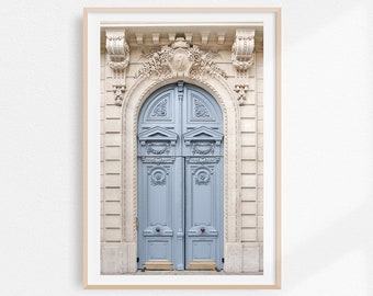May include: A photograph of a blue double door with ornate carvings, set within a stone archway. The door is framed by a light beige building with intricate details.