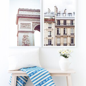 May include: Two framed photographs of Parisian architecture. The first photo shows the Arc de Triomphe, and the second photo shows a building with balconies and windows. A white bench with a blue and white striped throw blanket sits in front of the photos.
