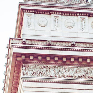 May include: A close-up view of the top of the Arc de Triomphe in Paris, France. The white stone archway is decorated with intricate carvings and sculptures. The top of the arch is adorned with a row of statues and a railing.