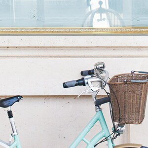 May include: A light blue bicycle with a wicker basket and a silver bell. The bicycle has a black seat and tires with tan sidewalls. The handlebars have gray grips. The text "*ZOOM VIEW" is in the top left corner.