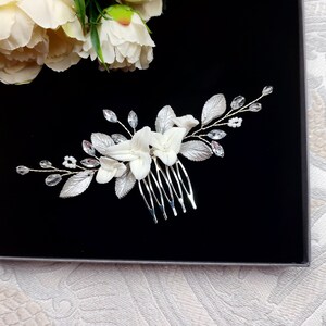 Peigne à cheveux floral avec fleurs blanches et feuilles argentées en porcelaine froide, cristal et strass transparent et perles de rocailles pour chignon ou coiffure de mariage bohème champêtre chic