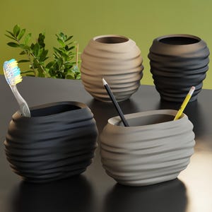 May include: Four decorative containers in shades of grey and beige. Two oval containers hold a toothbrush and pencils. Two round containers are in the background. The containers have a textured, wavy design.