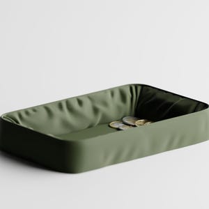 May include: An olive green rectangular tray with a textured interior and rounded corners. Several coins are inside. The tray is designed for organizing small items. The tray's dimensions are not visible.