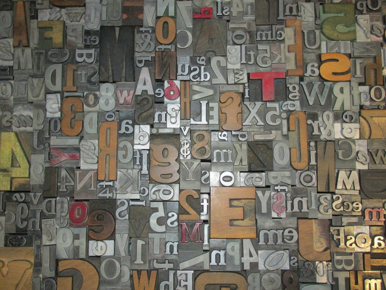 May include: A close-up of a collection of vintage letterpress printing blocks. The blocks are made of metal and wood, with various fonts and sizes. The letters and numbers are in different colors, including brown, red, and yellow.