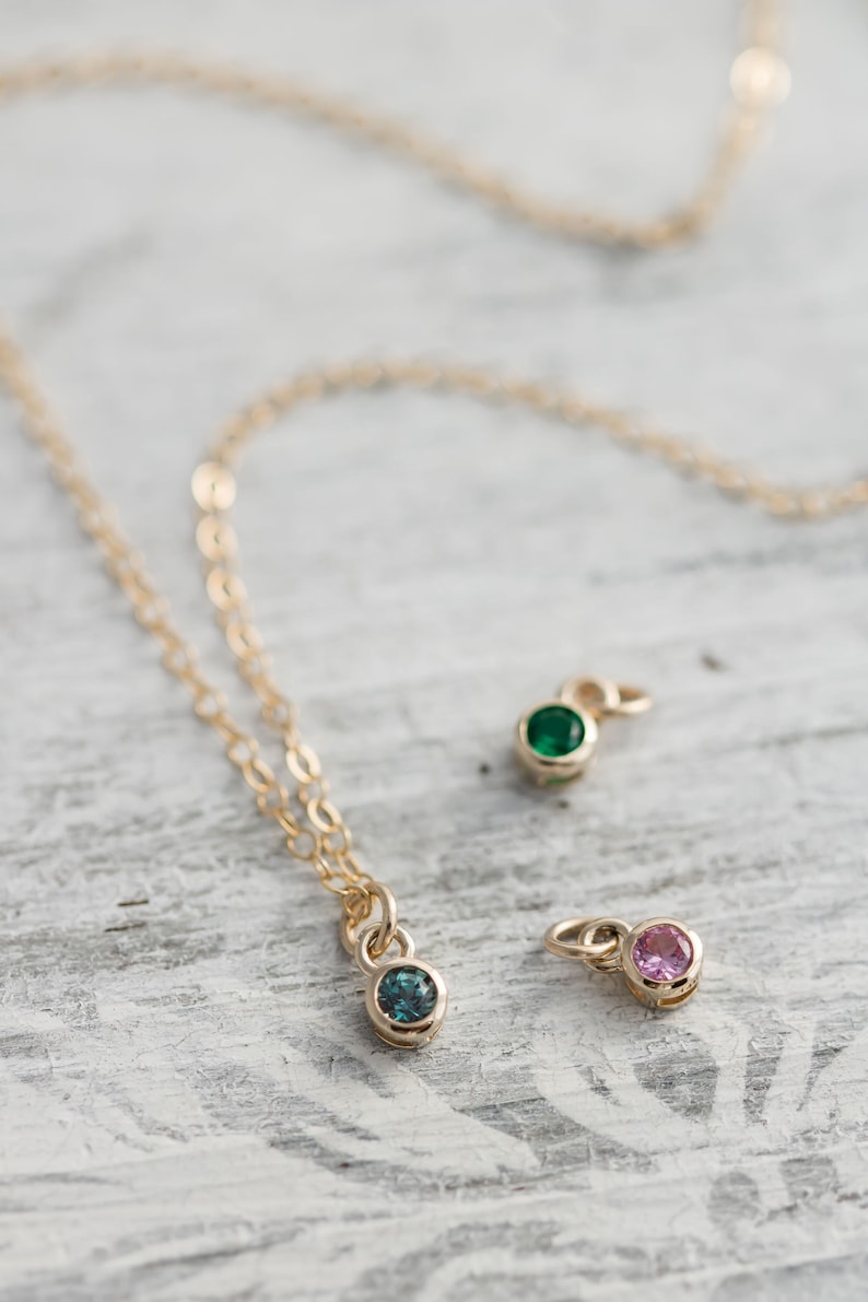 Pode incluir: Um colar de corrente de ouro com tr&ecirc;s pequenos pingentes, cada um com uma gema de cor diferente. Os pingentes s&atilde;o uma gema azul claro, uma verde e uma rosa.