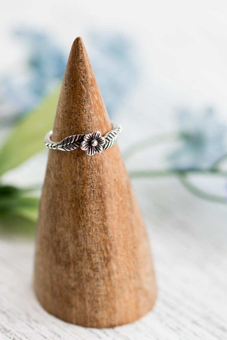 K&ouml;nnte beinhalten: Ein silberner Ring mit einem Blumen- und Blattdesign auf einem Holzringst&auml;nder.