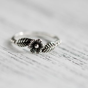 K&ouml;nnte beinhalten: Ein silberner Ring mit einem Blumen- und Blattdesign.