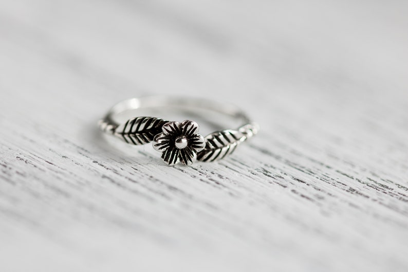 K&ouml;nnte beinhalten: Ein silberner Ring mit einem Blumen- und Blattdesign.