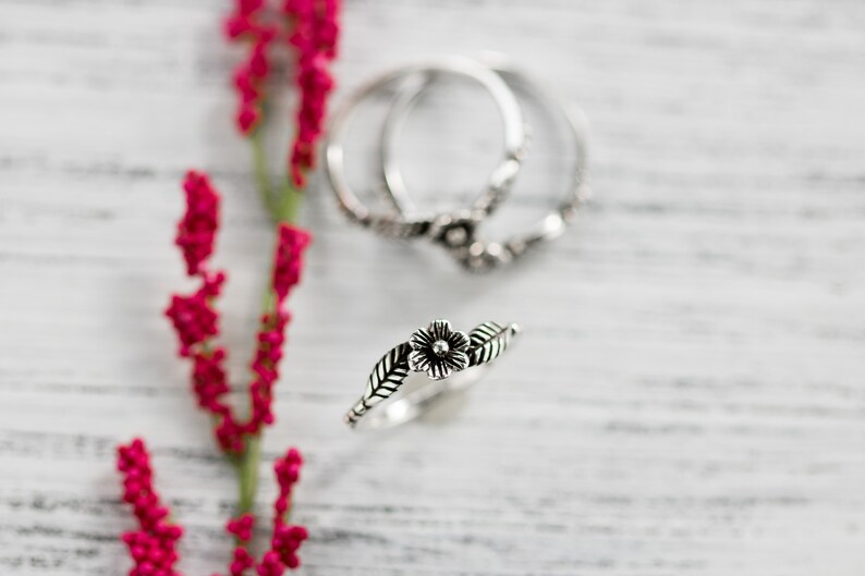 K&ouml;nnte beinhalten: Zwei silberne Ringe mit floralen Designs. Die Ringe sind &uuml;bereinander gestapelt. Der obere Ring hat eine einzelne Blume mit Bl&auml;ttern auf beiden Seiten. Der untere Ring hat ein filigraneres Blumenmuster.