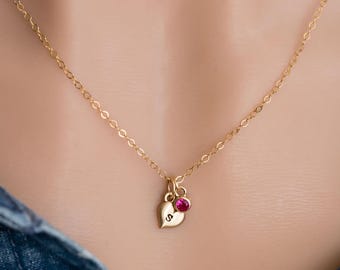 May include: A gold chain necklace with a small heart pendant and a single red gemstone. The heart pendant has a letter 'S' engraved on it.