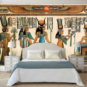 Puede incluir: Un mural de pared beige y marr&oacute;n que representa a cinco mujeres con ropa egipcia colorida. Las mujeres est&aacute;n de pie frente a un fondo jerogl&iacute;fico con un disco solar alado sobre ellas. El mural est&aacute; enmarcado por un borde blanco y se muestra en un dormitorio con una cama blanca y mesitas de noche blancas.