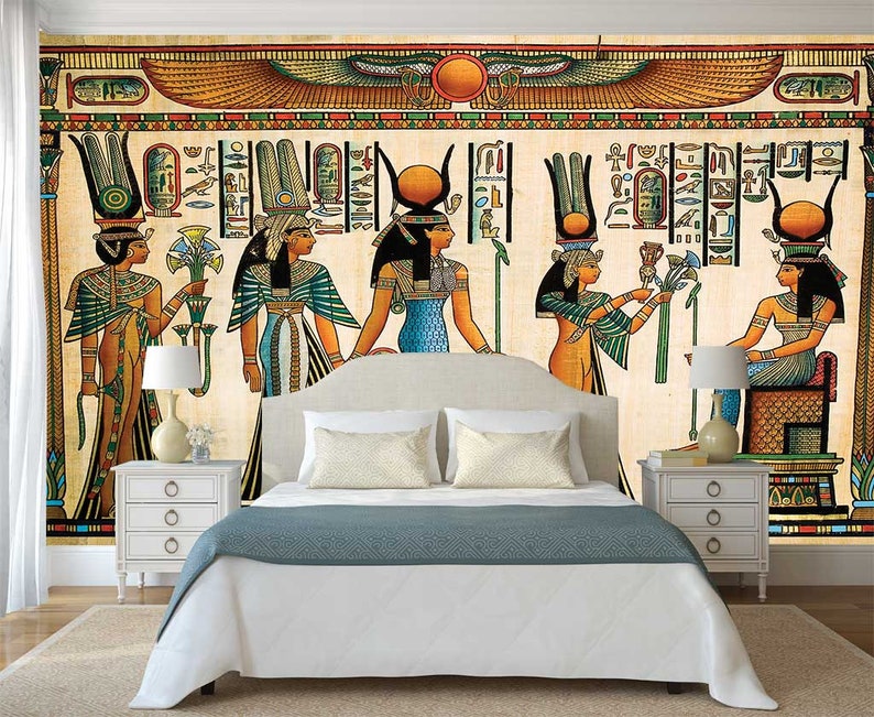 Puede incluir: Un mural de pared beige y marr&oacute;n que representa a cinco mujeres con ropa egipcia colorida. Las mujeres est&aacute;n de pie frente a un fondo jerogl&iacute;fico con un disco solar alado sobre ellas. El mural est&aacute; enmarcado por un borde blanco y se muestra en un dormitorio con una cama blanca y mesitas de noche blancas.