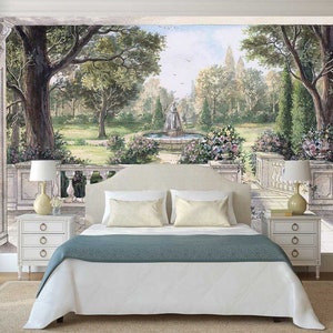 May include: A white bed with a teal blue bedspread sits in front of a wall mural depicting a garden scene with a fountain and trees. Two white nightstands with drawers are on either side of the bed.