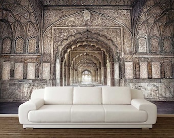 May include: A white couch sits in front of a photo mural depicting a long, ornate hallway with arched doorways and intricate stonework. The hallway is lined with columns and arches, creating a sense of depth and perspective.
