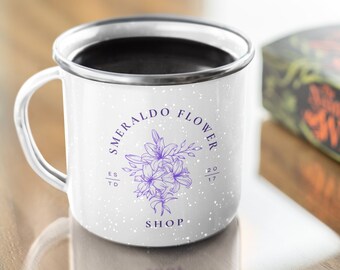 May include: White enamel camping mug with a black handle and a purple floral design. The mug has the text "SMERALDO FLOWER SHOP" and "EST 2017" printed on it.
