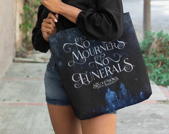 May include: A black tote bag with a blue and white design. The bag features the text "No Mourners. No Funerals." and the title "Six of Crows" by Leigh Bardugo.