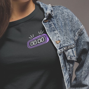 May include: A black t-shirt with a purple digital clock graphic that reads "00:00".