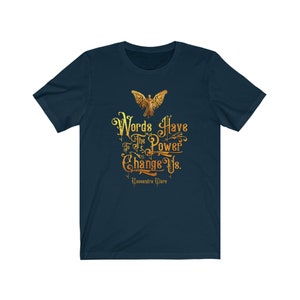 Puede incluir: Una camiseta azul marino con un gr&aacute;fico dorado de una figura alada y el texto "Words Have The Power To Change Us. Cassandra Clare".