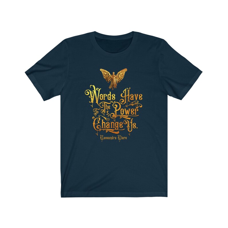 Puede incluir: Una camiseta azul marino con un gr&aacute;fico dorado de una figura alada y el texto "Words Have The Power To Change Us. Cassandra Clare".