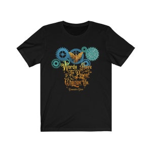 Puede incluir: Camiseta negra con un dise&ntilde;o gr&aacute;fico de engranajes y un &aacute;ngel con la cita "Las palabras tienen el poder de cambiarnos." de Cassandra Clare.