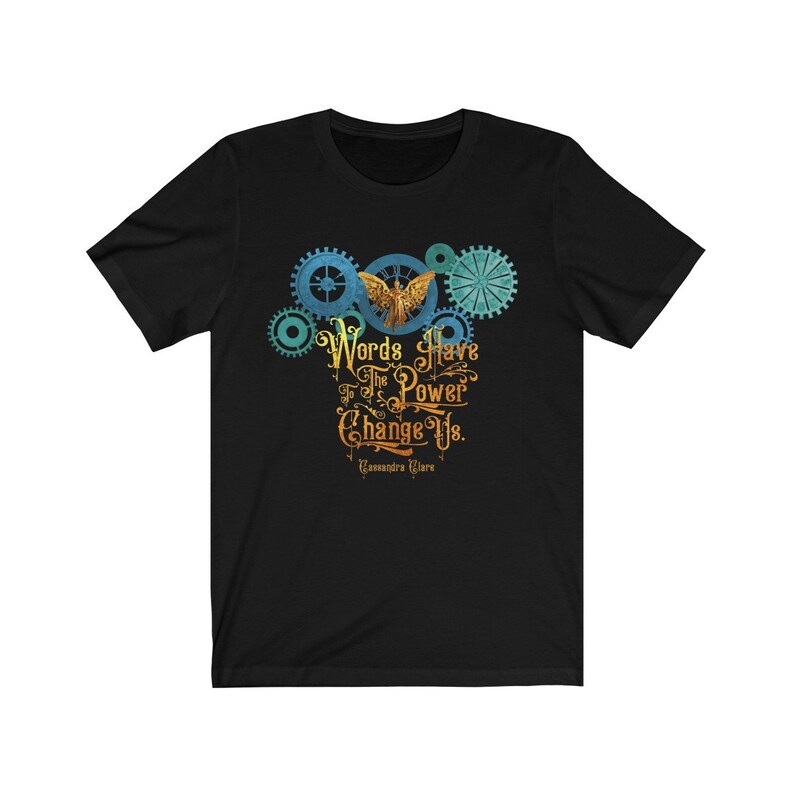 Puede incluir: Camiseta negra con un dise&ntilde;o gr&aacute;fico de engranajes y un &aacute;ngel con la cita "Las palabras tienen el poder de cambiarnos." de Cassandra Clare.